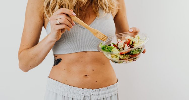 Young woman in sports attire holding a fresh salad bowl, promoting a healthy lifestyle.