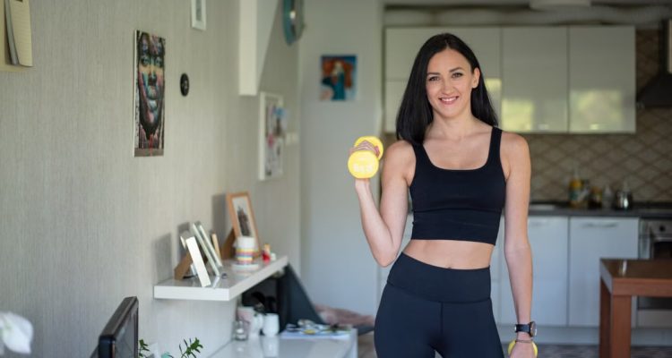 Smiling woman in activewear lifting dumbbells at home for a healthy lifestyle.